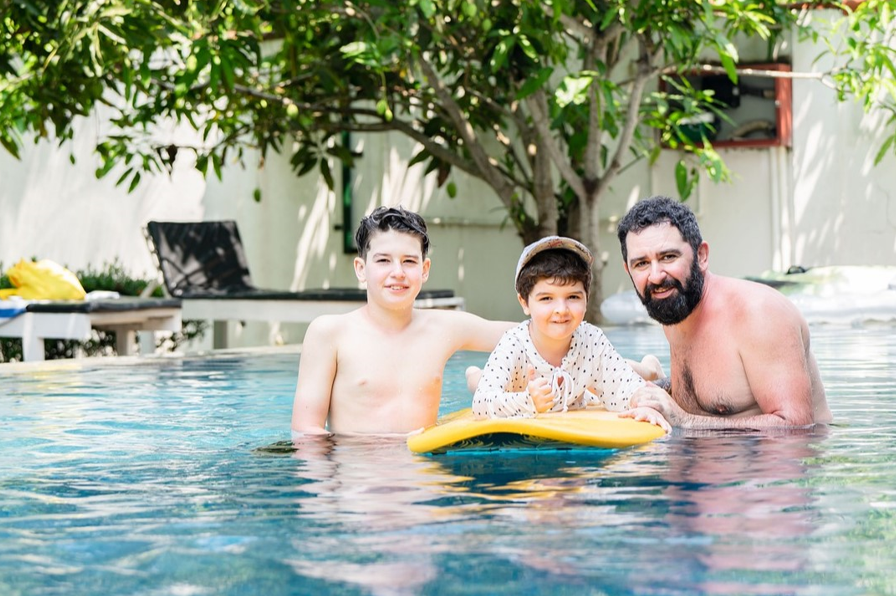 Dos niños y un adulto nadando en una piscina